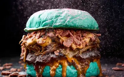 Una hamburguesa gigante con pan azul, carne jugosa, queso derretido y crujiente tocino, perfecta para un festival hamburguesa.