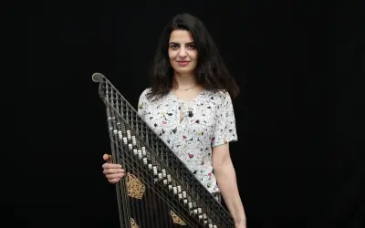 Une musicienne tient un kanoun, instrument de musique à cordes pincées, devant un fond noir.