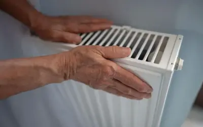 Manos sobre un radiador blanco, sintiendo el calor. El radiador hace ruido, quizás por el agua circulando.