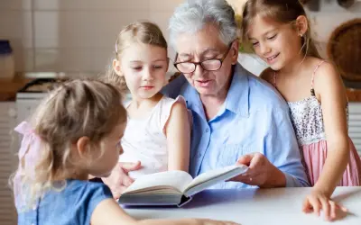 Babcia czyta książkę trzem wnuczkom przy stole.