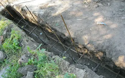 Zbrojenie do fundamentu ogrodzeniowego w wykopie. Metalowe pręty tworzą siatkę, gotową na zalanie betonem.