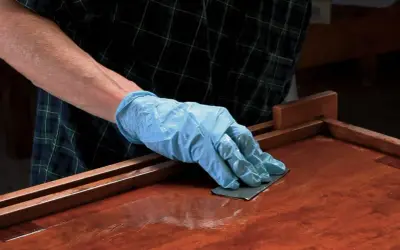 Mano enguantada lijando superficie de madera barnizada. El lijado es un paso clave para aplicar lac.