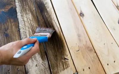 Aplicando tinte oscuro a madera sin tratar con una brocha. El proceso de pintar madera sin tratar transforma su aspecto.