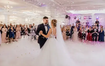 Para młoda tańczy na weselu, goście patrzą, zespół gra. W tle konfetti i dym. Piękny moment, ale czy wiesz o ukrytych kosztach wesela?