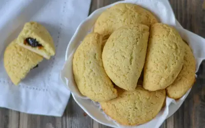 Dolci tipici bologna: biscotti dorati ripieni di marmellata, serviti in una ciotola bianca su un tovagliolo.