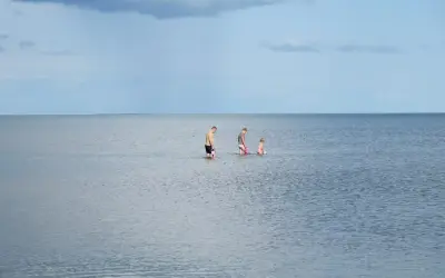 Rodzina brodząca w spokojnym morzu, na tle błękitnego nieba z chmurami.