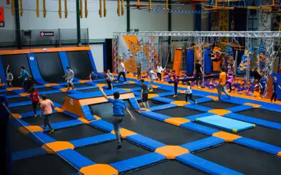 Dzieci skaczą na trampolinach w największym parku trampolin w Polsce. W tle widać ściankę wspinaczkową i tor przeszkód.