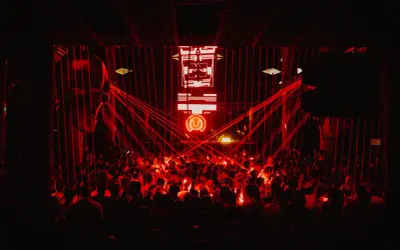 Multitud vibrante en un club nocturno, bañada en luces rojas. El logo de "Circus Nation" ilumina el escenario.