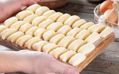 Ania gotuje pierogi leniwe. Na desce ułożone są rzędy gotowych do gotowania pierogów leniwych.