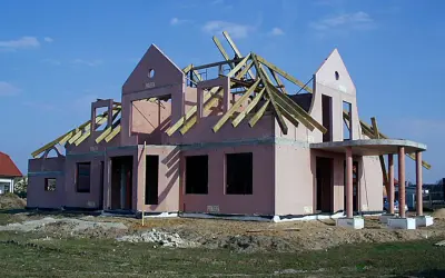 Budowa domu keramzytowego w różowym tynku, z widoczną konstrukcją dachu i wejściem z kolumnami.