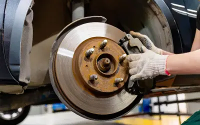 Gros plan sur un disque de frein rouillé et une plaquette de frein usée, tenue par une main gantée, prête pour le remplacement.