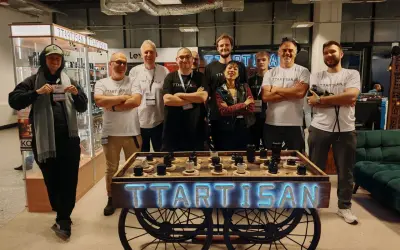 Grupa osób pozuje przy stoisku TTARTISAN z obiektywami.