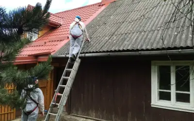 Pracownicy w kombinezonach zabezpieczających usuwają eternit z dachu. To pokazuje, co to jest azbest i jak wygląda jego utylizacja.