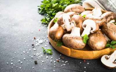 Brązowe pieczarki w drewnianej misce z natką pietruszki i solą na czarnym tle.