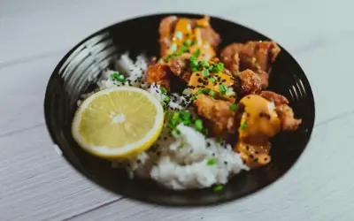 Chrupiące karaage z ryżem, posypane sezamem i szczypiorkiem, podane z plasterkiem cytryny.