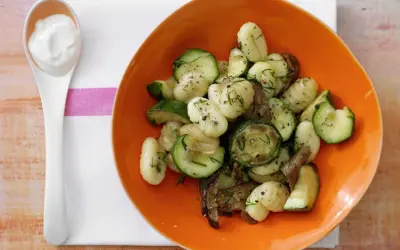 Gnocchi mit Zucchini und Pilzen in einer orangen Schüssel, dazu ein Löffel cremiger Dip. Eine köstliche zucchini pfanne.