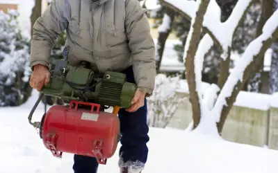 Mężczyzna w zimowej scenerii trzyma pompę, przygotowując się do zadania, jak wypompować wodę ze zbiornika na deszczówkę.