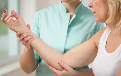 Une thérapeute examine le bras d'une patiente, possiblement pour une nevralgie cervico brachiale.