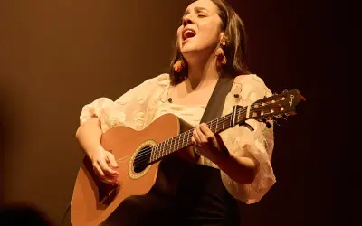 Valeria Castro Zaragoza canta con pasión, guitarra en mano, bajo una luz cálida.