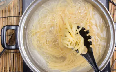 Spaghetti kochen in sprudelndem Wasser. Ein schwarzer Pastalöffel hebt eine Portion heraus, um zu zeigen, wie kleben spaghetti nach dem kochen nicht zusammen.