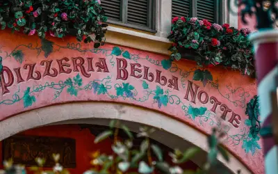 Różowa fasada Pizzerii Bella Notte ozdobiona winoroślą i kwiatami.