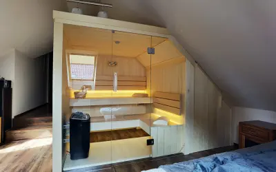 Nowoczesna sauna w domu, wykonana z jasnego drewna, z przeszklonymi drzwiami i nastrojowym oświetleniem. Idealne miejsce na relaks.