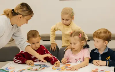 Nauczycielka pomaga dzieciom w przedszkolu układać puzzle. W Polsce przedszkole trwa zazwyczaj 5 lat.