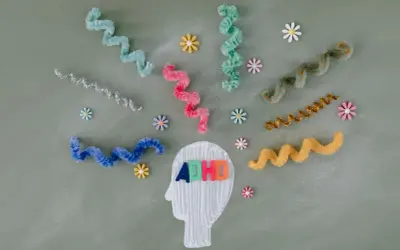 Kolorowe litery "ADHD" w głowie symbolizują diagnozę. Wirujące wstążki i kwiatki odzwierciedlają natłok myśli.