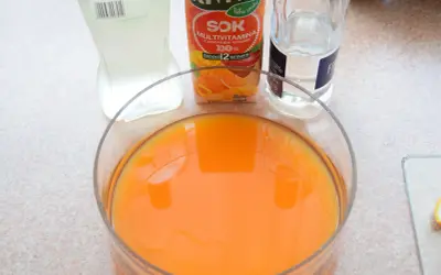 Pomarańczowy sok w dużej misie, obok karton soku multivitamin i butelka wody. Idealne składniki na orzeźwiający **jungle juice**.