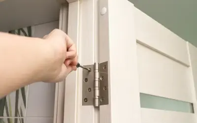 Dłoń dokręca śrubę w zawiasie drzwi, wykonując regulację zawiasów drzwi.