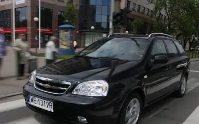Czarny Chevrolet Lacetti kombi jedzie ulicą, mijając budynki i przechodniów.