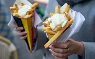 Dwie porcje frytek w papierowych rożkach, polane gęstym, białym sosem.