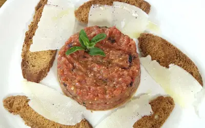 Tartar de tomate fresco, servido con finas láminas de queso y tostadas crujientes. Un bocado ligero y lleno de sabor.