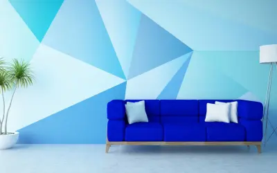 Niebieska sofa stoi przed ścianą pomalowaną do połowy w geometryczne wzory. Obok stoi lampa i roślina.