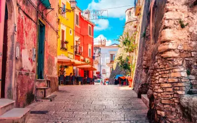 Vico del Gargano, Vicolo del Bacio: un vicolo pittoresco con case colorate, tavolini all'aperto e un'antica muraglia di pietra.