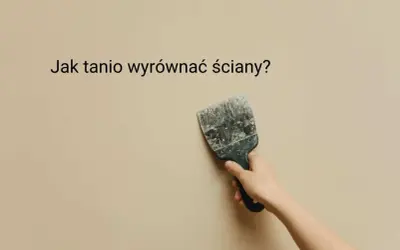 Dłoń trzyma szpachelkę przy lekko nierównej, beżowej ścianie. Jak tanio wyrównać ściany?