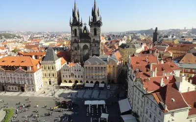 Blick über die Dächer der **Prag Stadt** mit der Teynkirche im Zentrum. Menschen beleben den Platz.