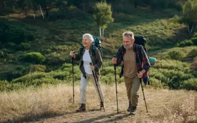 Uśmiechnięta para seniorów z plecakami przemierza leśny szlak, ucząc się, jak chodzić z kijkami.