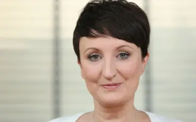 Agnieszka Burzyńska zmagająca się z chorobą, patrzy w obiektyw z delikatnym uśmiechem.