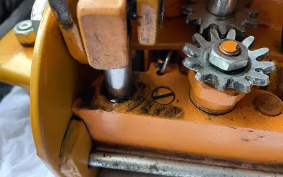 Zbliżenie na mechanizm zębatkowy pomarańczowego lewarka z widocznymi śladami oleju.
