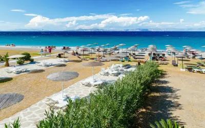 Słoneczna plaża Faliraki by Sun Palace z leżakami i parasolami. Turkusowe morze i góry w tle.