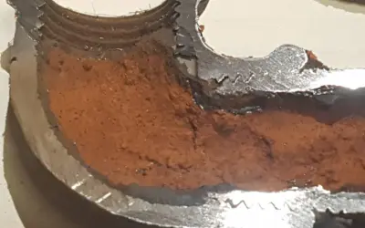 Sezione di tubo metallico con incrostazioni marroni che mostrano come evitare la formazione di calcare nelle tubazioni.