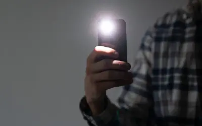 Dłoń trzyma smartfon z włączoną latarką. Dowiedz się, jak wyłączyć latarkę w telefonie, aby oszczędzać baterię.