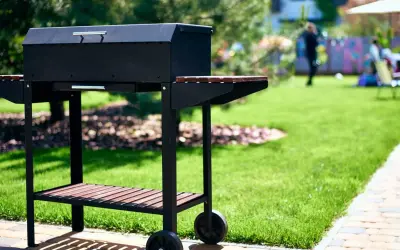 Czarny grill na kółkach w ogrodzie, gotowy na przyjęcie gości. Idealny pomysł na to, co na grilla tanio i smacznie.