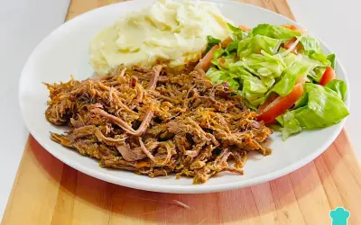 Plato de carne mechada jugosa, puré de papas cremoso y ensalada fresca de lechuga y tomate.