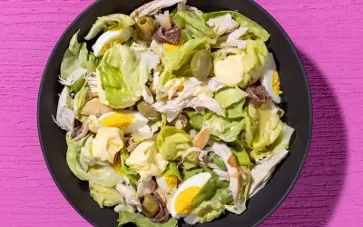 Insalata di pollo ricca con lattuga, uova sode, olive verdi e acciughe, condita con maionese.