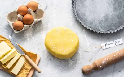 Impasto giallo per pasta frolla senza glutine, uova, burro e stampo per crostata pronti per creare un dolce delizioso.