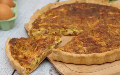 Une part de quiche lorraine dorée, avec sa garniture aux lardons et herbes, prête à être dégustée. La vraie recette quiche lorraine.