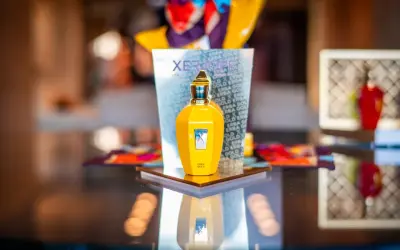 Żółta butelka perfum Xerjoff Erba Gold na lustrzanym blacie, odbijająca się w tafli.
