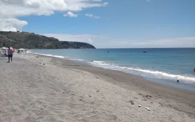 Piękna plaża na wyspie Dominika. Ciemny piasek, turkusowe morze i zielone wzgórza w tle. Idealne miejsce na relaks.